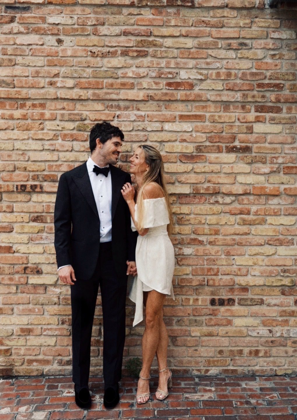 Hunter and Mary smiling at each other against a brick wall