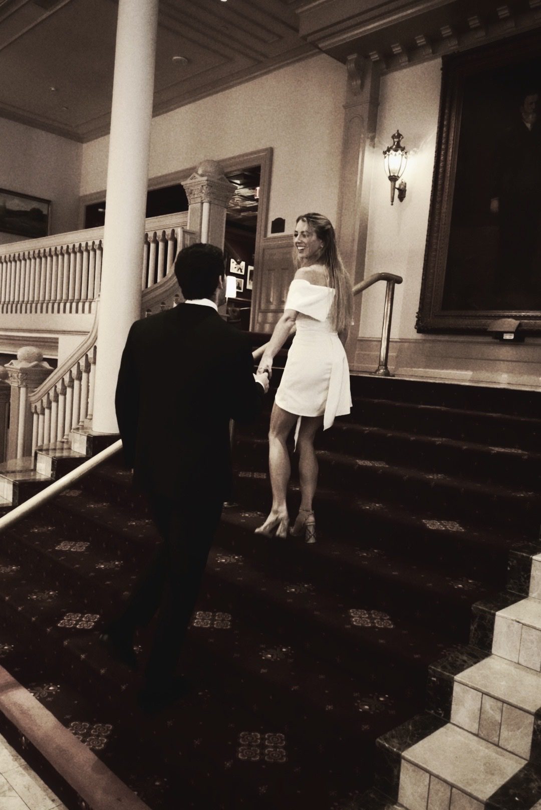 Mary looking back at Hunter as they hold hands on a staircase
