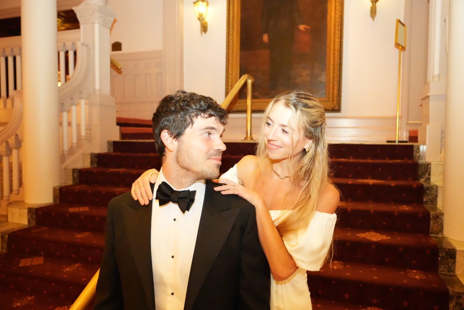 Mary resting her hands on Hunter's shoulders on the staircase